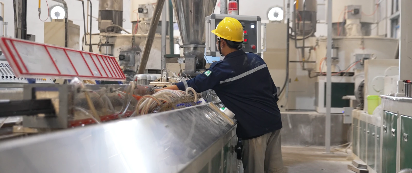 Operator berhelm kuning bekerja pada mesin produksi di pabrik.